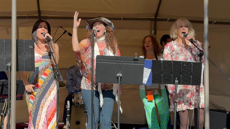 Three Enjoyus vocalists performing at an outdoor tent stage